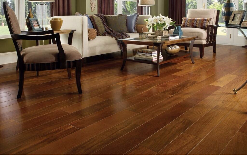 A cozy living room with warm-toned hardwood flooring, striped armchairs, and a comfortable sofa, complemented by soft, natural light streaming through large windows.