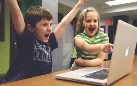 Two excited children celebrating while using a laptop together at a table.